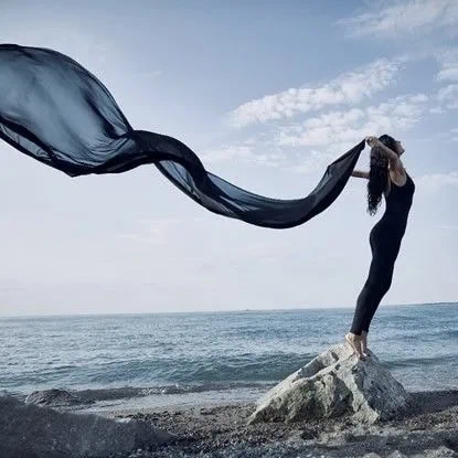 Women with blue scarf standing on a stone near beach feeling free and letting go