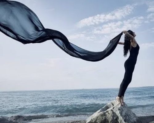 Women with blue scarf standing on a stone near beach feeling free and letting go