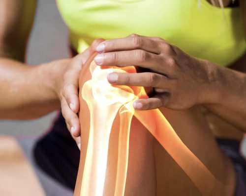 Low section of sportswoman suffering from knee pain while sitting on track during sunny day