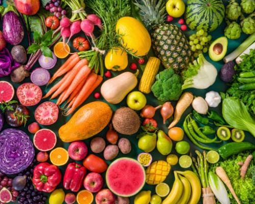 Colorful raw fruits and vegetables varied vegan food, vivid rainbow arrangement full frame background